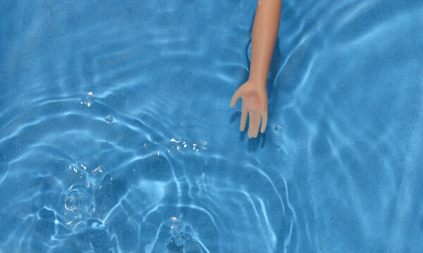 Doll hand in blue water with shadows.
