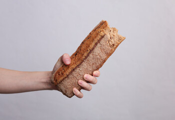 Female hand holding broken rye baguette on a gray background