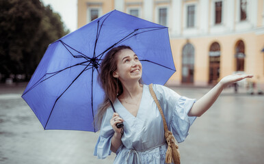 Young smiling woman in dress with umbrella waiting for rain in the city