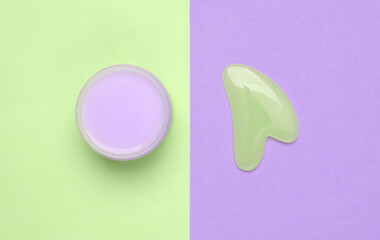 Cream jar and gua sha stone massager on colored background. Top view