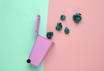 Miniature trash can with crumpled paper balls on blue-pink pastel background. Recycling concept. Top view