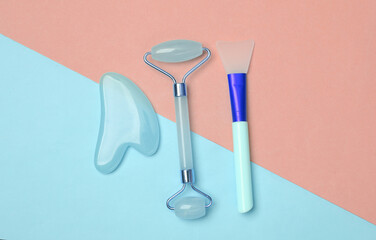 Face roller and gua sha stone massager, brush on pink blue background. Top view