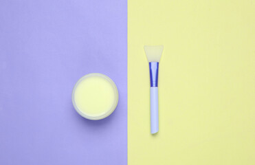 Jar of cream and brush on colored background