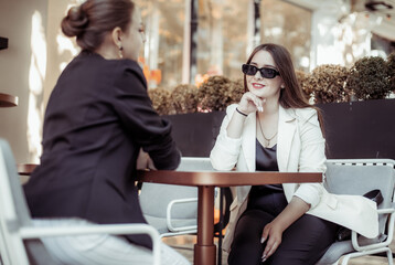 Two cute women friend talking while discussing while sitting at table in outdoor cafe