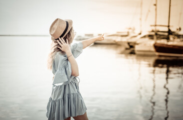 A cute young woman in a plaster and a hat looks at the yacht club