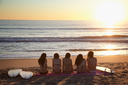 Backview of Young Women with Surfboards, Sitting on Beach watching Sunset, Zuma Beach, California, USA