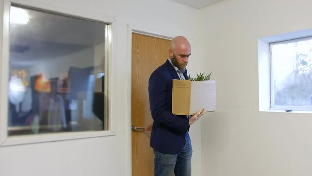 A man leaving work after being fired from his job. He is walking out of the office with a box of his belongings