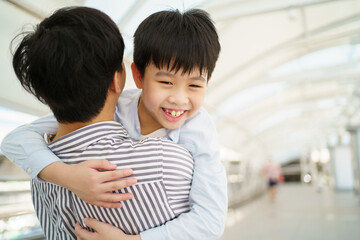 Happy cheerful Asian little boy running to his father at the railway or sky train station after his father.