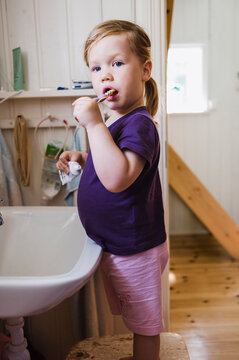 2 year old girl brushing her teeth at the sink in the bathroom looking at camera, Sweden