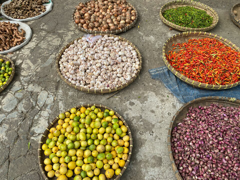 various vegetables tomatoes, chilli, red onion, corn, carrot, lime, garlic being sold at asian traditional market. colorful vegetables on round bamboo tray at traditional market floor