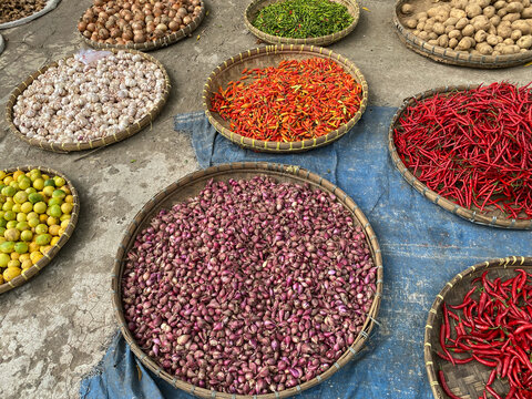 various vegetables tomatoes, chilli, red onion, corn, carrot, lime, garlic being sold at asian traditional market. colorful vegetables on round bamboo tray at traditional market floor