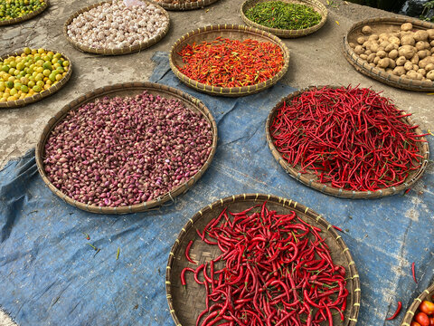 various vegetables tomatoes, chilli, red onion, corn, carrot, lime, garlic being sold at asian traditional market. colorful vegetables on round bamboo tray at traditional market floor