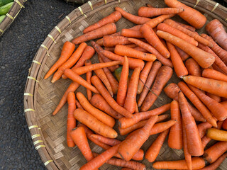 fresh, organic and imperfect carrots on round bamboo tray being sold at traditional market