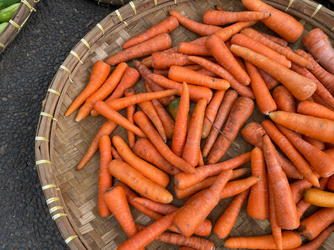 fresh, organic and imperfect carrots on round bamboo tray being sold at traditional market