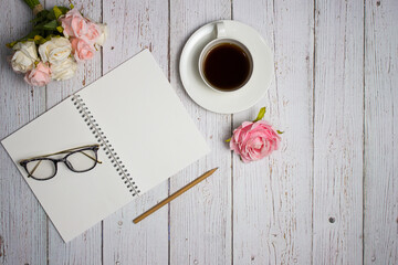 Notebook with coffee, glasses, pen and flowers over the wooden table. 