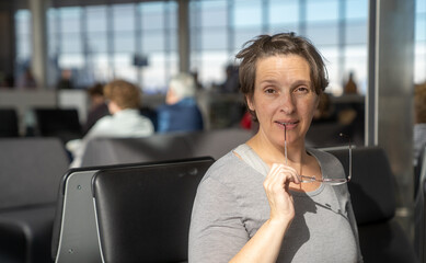 Woman at an airport waiting for flight with glasses in her mouth