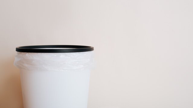 Empty white trash can with a package on a light background with copy space