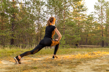 woman warms up before jogging near a road in the forest. A healthy woman warms up before running and relaxes by stretching her arms. runner people workout fitness background.health and wellness