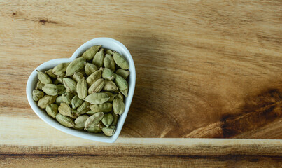 cardamom in heart shape bowl with wooden background 