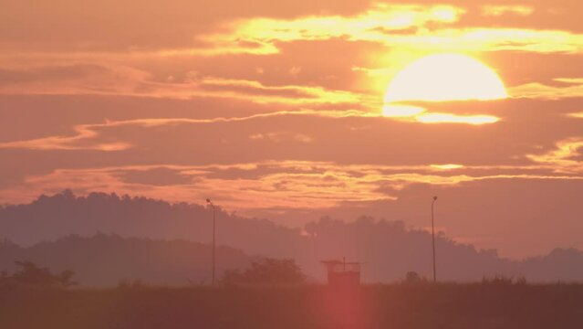 Daybreak in the morning is marked by the large sun rising gradually from above the horizon. In the winter morning, the sun rises amid a hazy sky and a mountain. Dawn sunrise on the natural landscape.