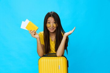 Asian woman traveling with yellow suitcase and tickets with passport in hand, tourist traveling by plane and train with luggage on blue background