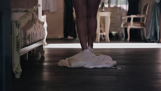 The girl in the bedroom throws off her clothes on the floor and goes forward. The camera shoots her legs from behind