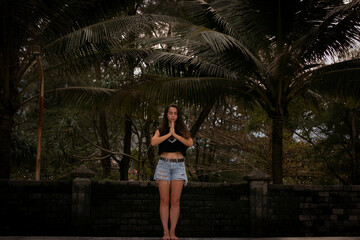 the girl stands and makes namaste. Yoga and meditation on the beach under palm trees. dark photo processing