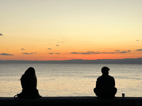 夕暮れの海を眺めて離れて座る男女のシルエット