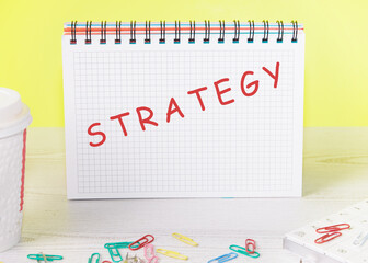 A word Strategy written on a sheet of a notebook in a check on a yellow background