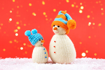 Two knitted snowmen on a red Christmas background in blue and orange knitted hats. Merry Christmas and New Year 2023 greeting card