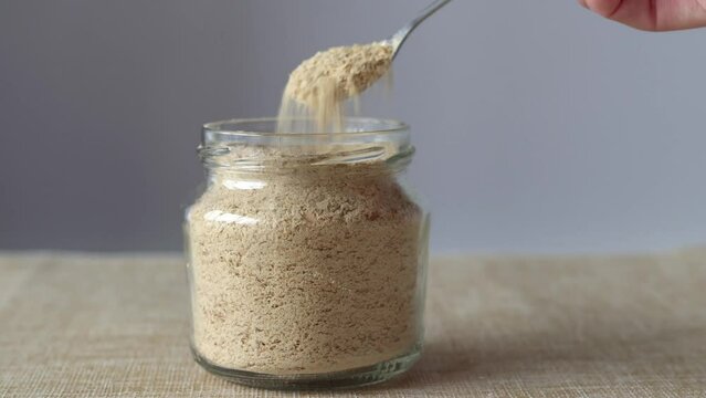 Nutritional Inactive Yeast in Glass Jar and Spoon In Female Hand., Side View. Flakes of Yellow Nutritional Yeast a Cheese Substitute and Seasoning for Vegan Cooking