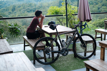 A young female cyclist having a cup of coffee at a cafe by the mountains.