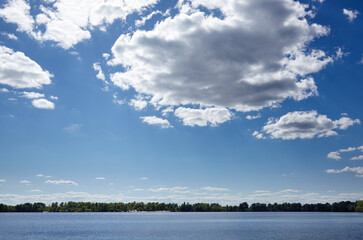 Beautiful river landscape. Lake surface on a sunny perfect day. The surface of the water against the background of trees and a blue sky. Blurred image, selective focus