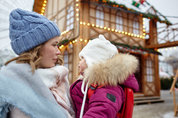Mother and daughter are walking around the city on Christmas and New Year holidays. Parent and little child having fun outdoors