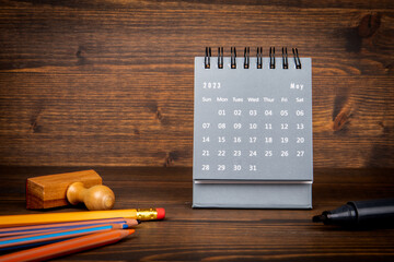2023 May. Desk calendar and office supplies on wooden texture background