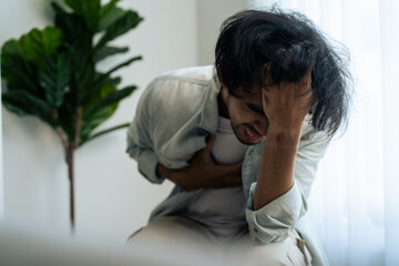 Asian young upset depressed man sitting alone in living room at home. 