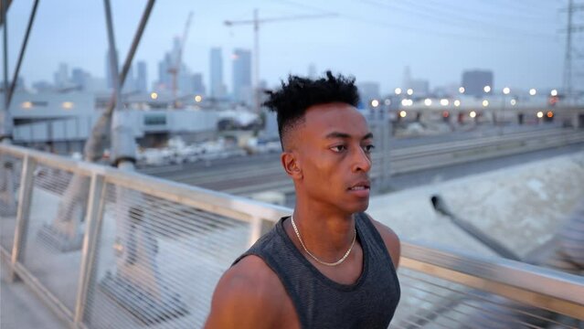 African American man working out by jogging across the 6th Street Bridge in Los Angeles at dawn on an overcast morning. Downtown LA can be seen in the background. Jogger has a deformed left hand.