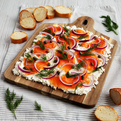 Homemade Cream Cheese Lox Bagel Board with Salmon on a white wooden surface, low angle view.