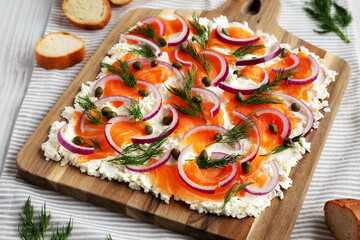 Homemade Cream Cheese Lox Bagel Board with Salmon on a white wooden surface, side view.