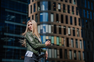 Fototapeta premium Beautiful hipster female standing on chairs outside against business center enjoys sunny day. Attractive young woman tired, walking, waiting for boyfriend. City and people. Perplexed female.
