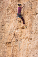 The girl climbs the rock. The climber is training to climb the rock. A strong athlete overcomes a difficult climbing route. Extreme hobby. A woman goes in for sports in nature.