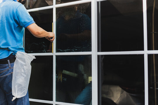 Worker use scraper cleaning window before installing tinting film.
