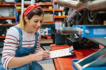 Portrait of smiling mechanic woman with clipboard filling out motorcycle documentation on garage