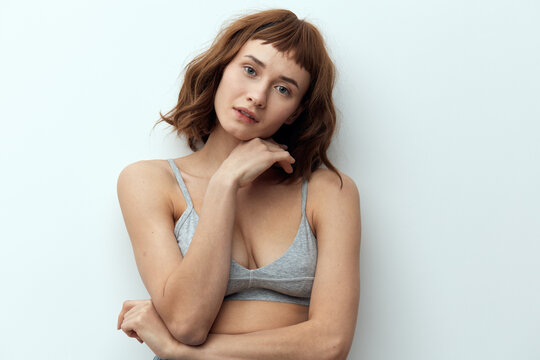 a sweet, thoughtful woman with red hair stands against a light background and poses relaxed touching her face with her hand. Studio photo with an empty space for inserting an advertising layout