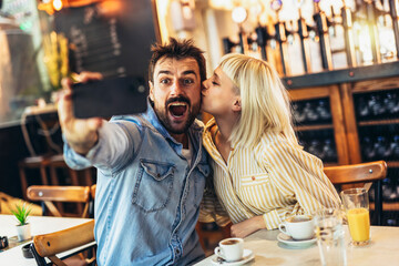 Young happy couple using smartphone to make selfie photo in cafe