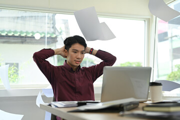 Image of stressed man office worker feeling distressed anxious with work deadline, sitting at desk with falling paperwork