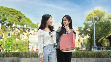 Fototapeta premium Image of two young asian women talking, spending time together while walking in the shopping district of a city