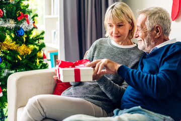 Romantic sweet senior couple having fun and smiling while celebrating enjoying valentines day time together.Senior man giving gift box surprise to wife in valentines day at home.