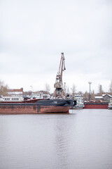 Fototapeta premium River port. Port cranes on the bank of the river. Embankment of the river port, a barge at the quay wall. Large port cranes on the river. Extraction and transportation of sand other cargo