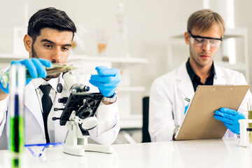 Professional two scientist man research and working doing a chemical experiment while making analyzing and mixing liquid in test tube.Young science man dropping sample chemical on glass at labor